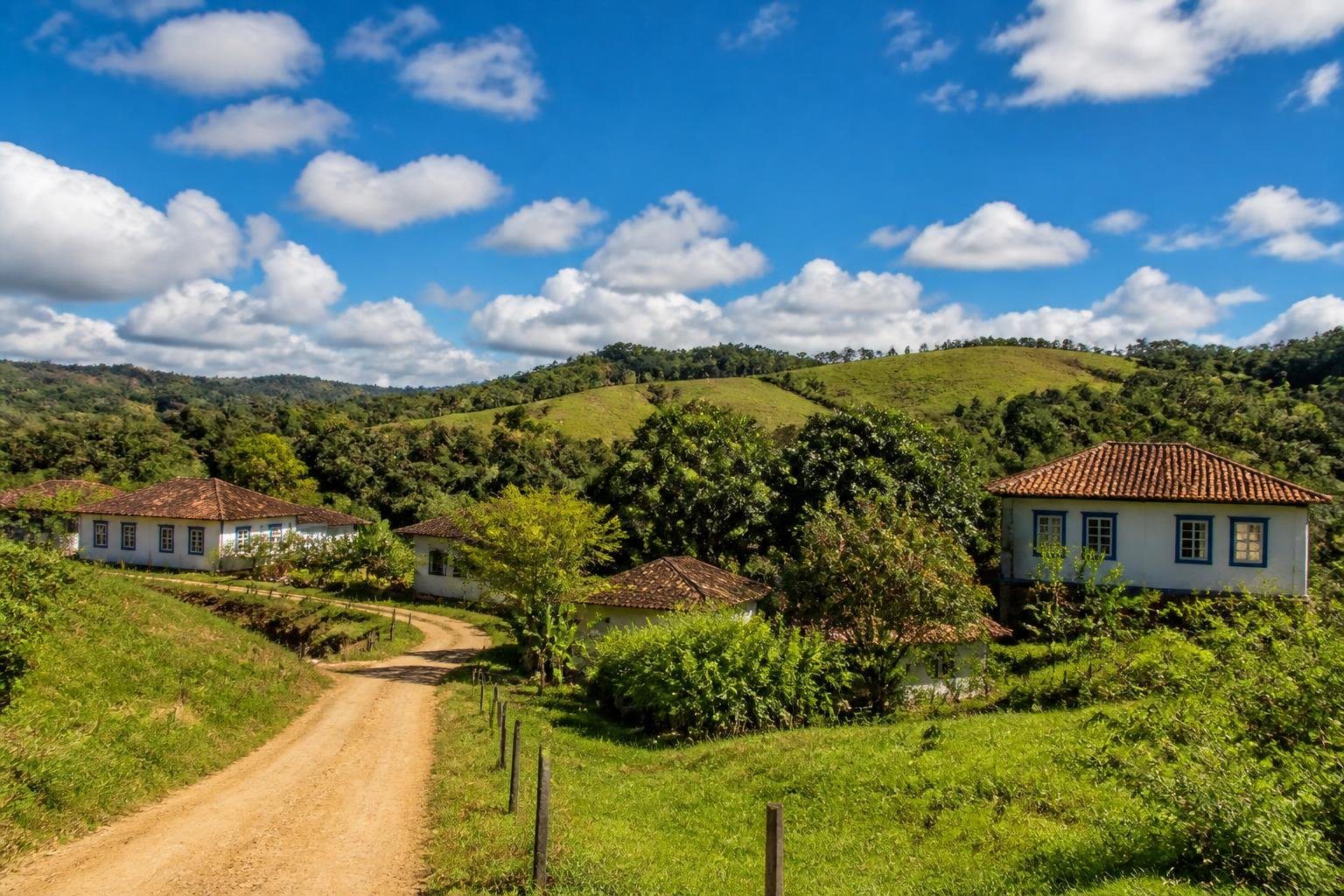 Paisagem rural de Santana dos Montes com colinas verdes, casas coloniais de telhado vermelho e céu azul claro.