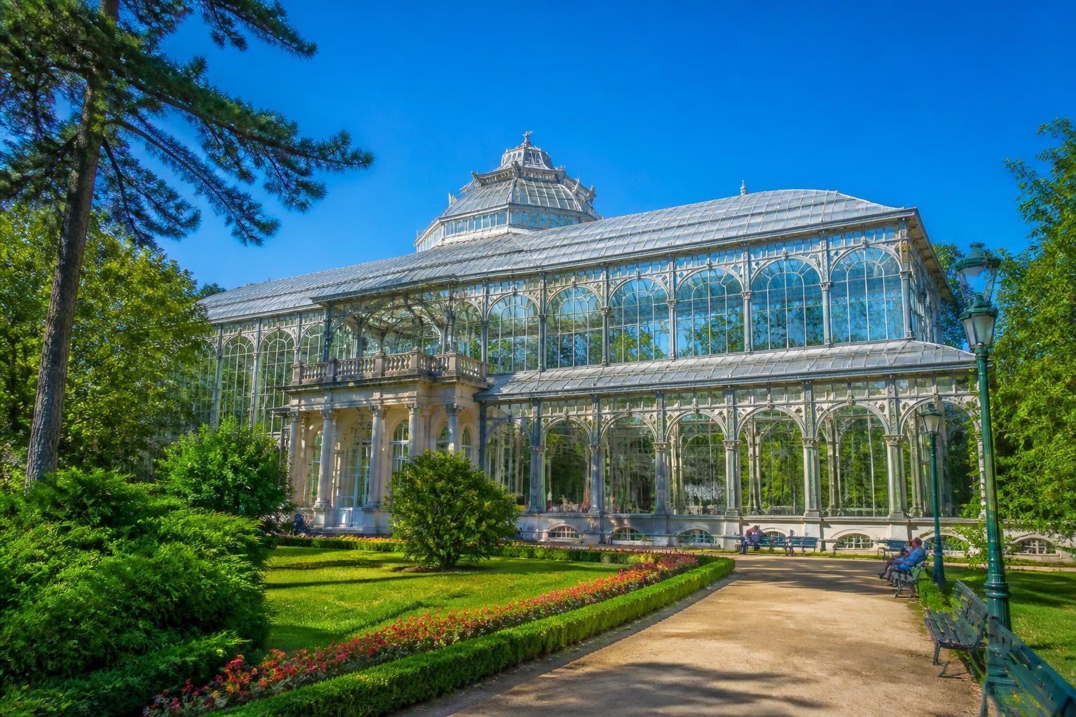 Palácio de Cristal em Porto cercado por jardins verdes com flores coloridas e pessoas caminhando sob um céu azul claro.