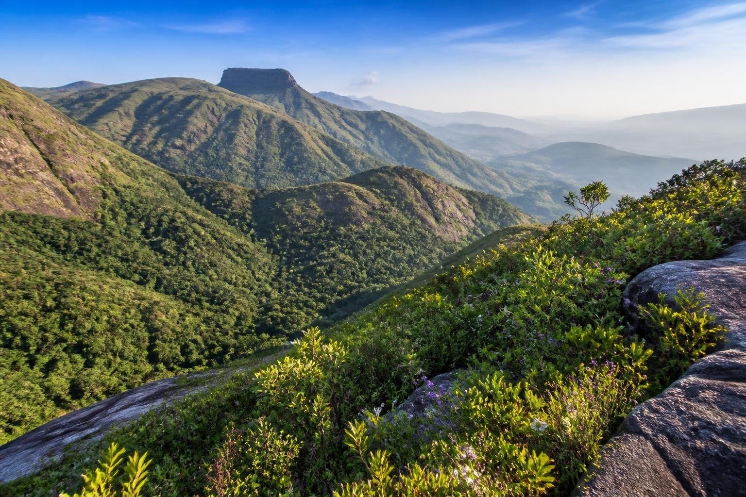 Vista panorâmica das montanhas verdes da Serra em Minas Gerais com céu azul claro e vegetação densa.