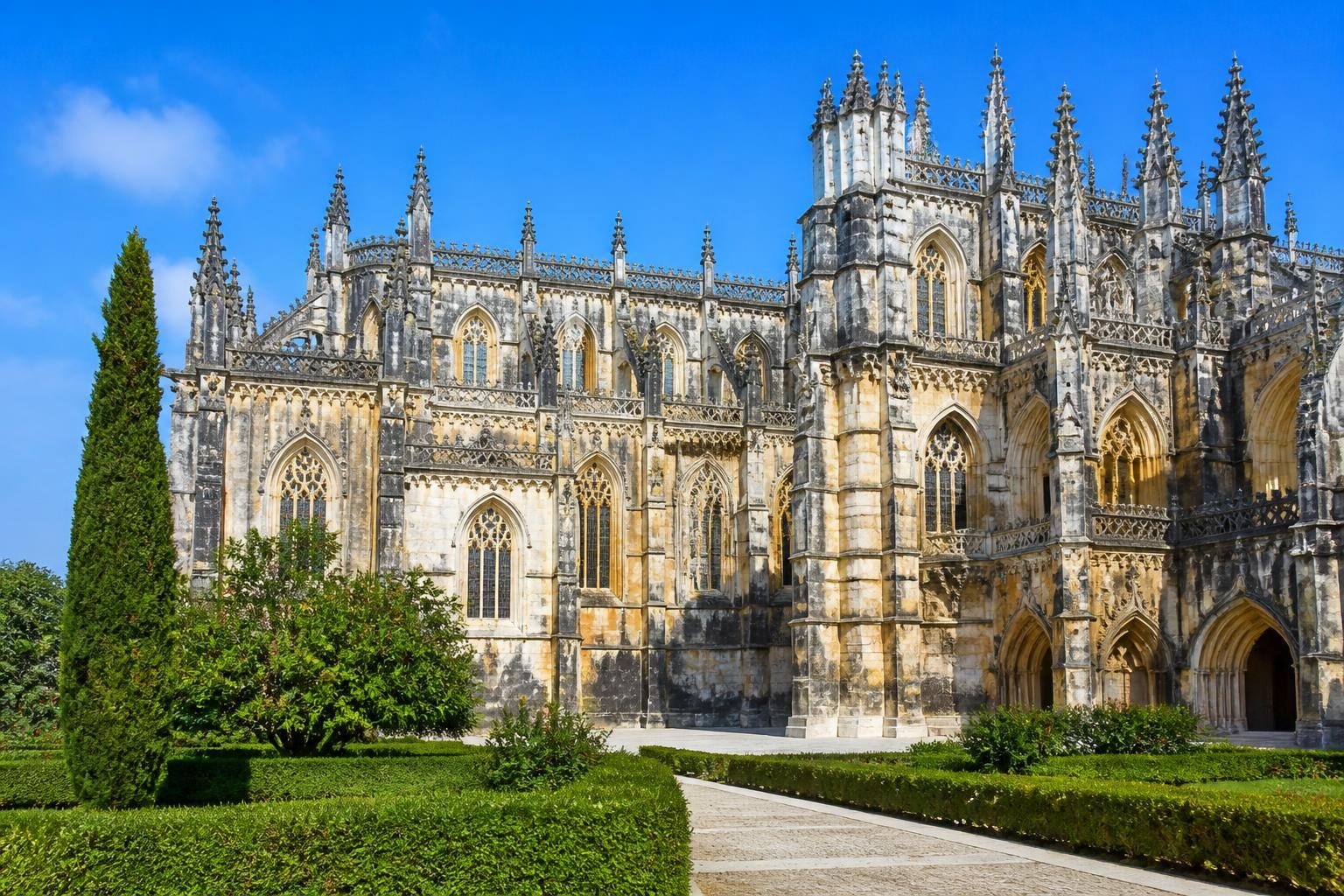 Mosteiro da Batalha com arquitetura gótica e manuelina, cercado por jardins e céu azul.