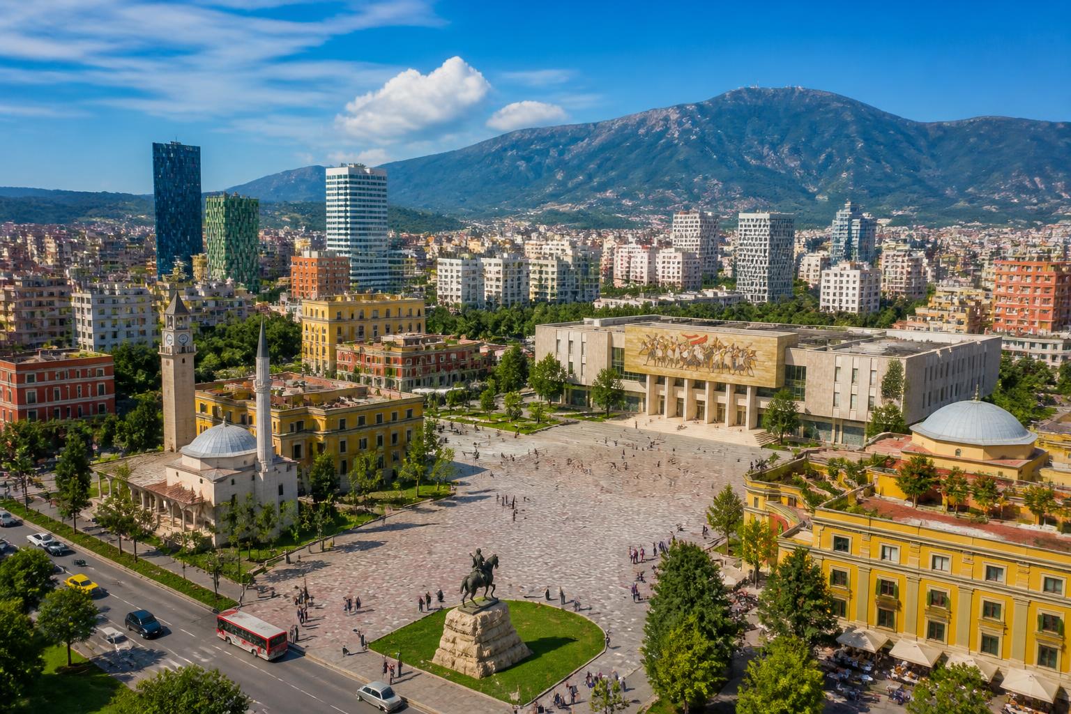 Vista da cidade de Tirana com a praça central, edifícios históricos e modernos, pessoas caminhando e montanhas ao fundo.